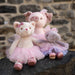 Three plush toys, including a bear, pig, and elephant, wearing tutus, sitting on a stone surface with a stone wall background.