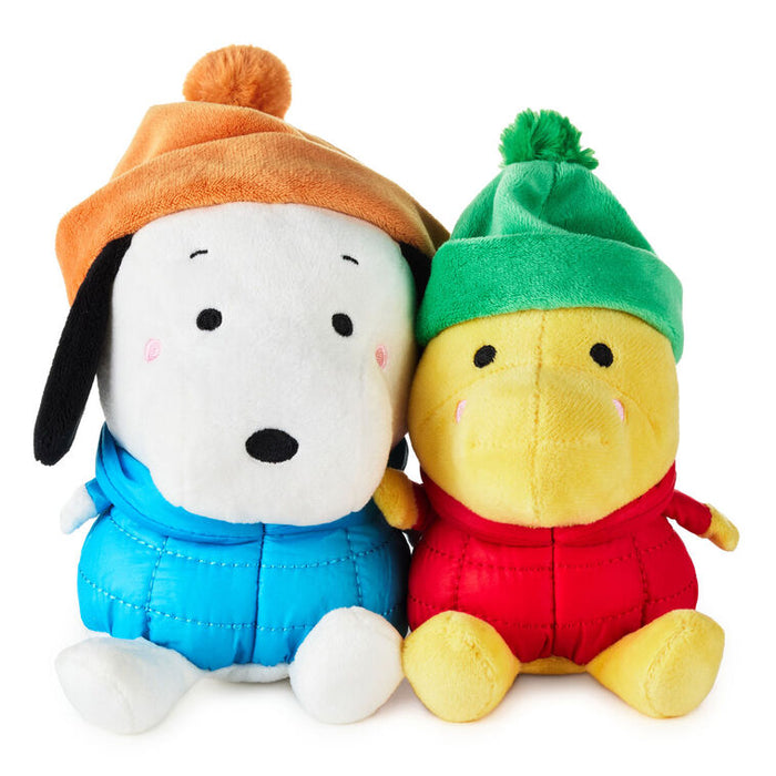 Two plush toys, one white with an orange hat and blue outfit, the other yellow with a green hat and red outfit, on a white background.