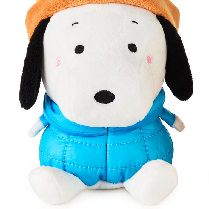 Plush toy resembling a dog with a blue outfit and orange hat on a white background