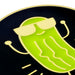 A close-up of a circular black enamel pin featuring a bright green pickle character wearing pale yellow sunglasses, with simple yellow line details and a gold-toned border.