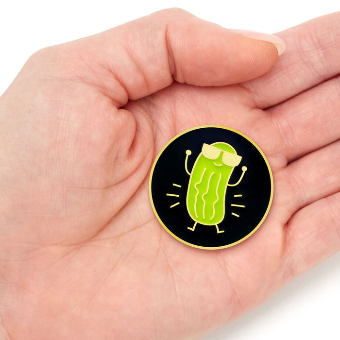 Hand holding a pickle-shaped pin with a black background