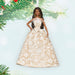 Barbie doll in a beige and white patterned dress with Christmas tree branches in the background