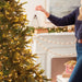 Person decorating a Christmas tree with lights and ornaments in a festive living room.