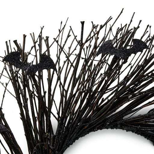Black artificial bare tree branches with two glittery bat decorations on a white background.