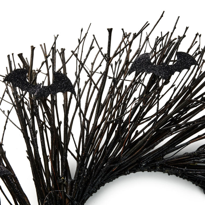 Black artificial bare tree branches with two glittery bat decorations on a white background.