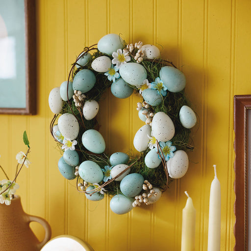 Decorative wreath with eggs and flowers on a yellow wall