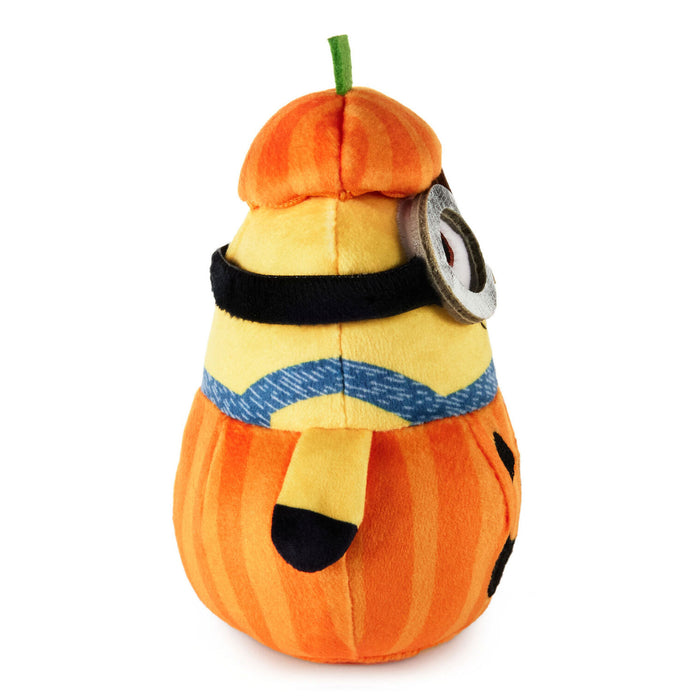 A plush Minion character toy styled as a pumpkin, featuring orange and yellow striped fabric, a black eye patch, a blue harness, and a green stem on a white background.