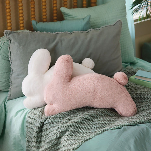 Pink and white plush toy on a bed with green bedding and pillows.