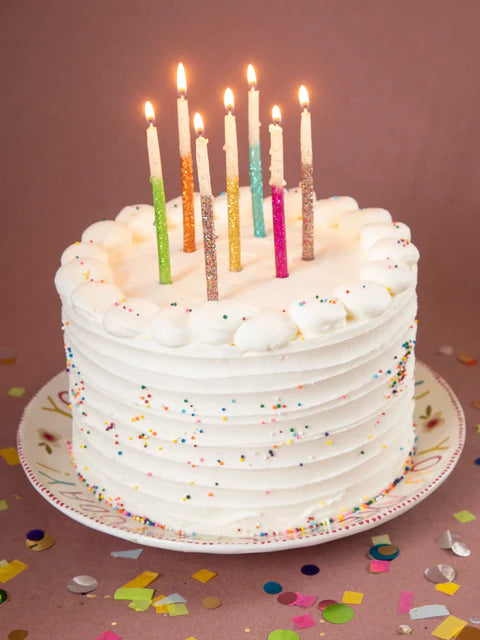 White birthday cake with colorful candles on a pink background