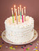 White birthday cake with colorful candles on a pink background