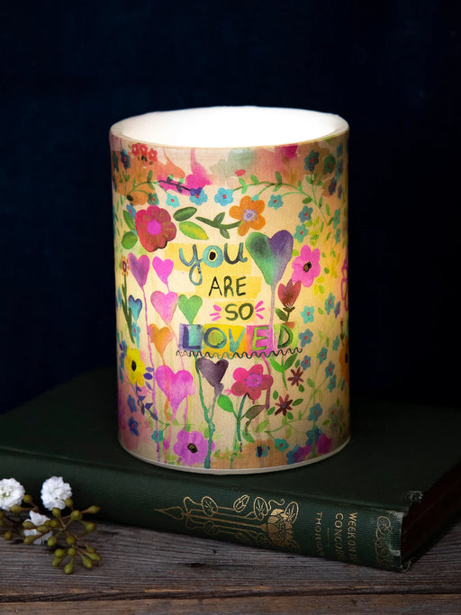 Colorful candle with floral design and 'You are so loved' text on a dark background