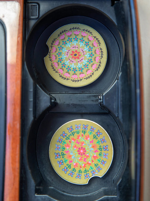 Two circular coasters with floral patterns on a black stand inside a wooden box.