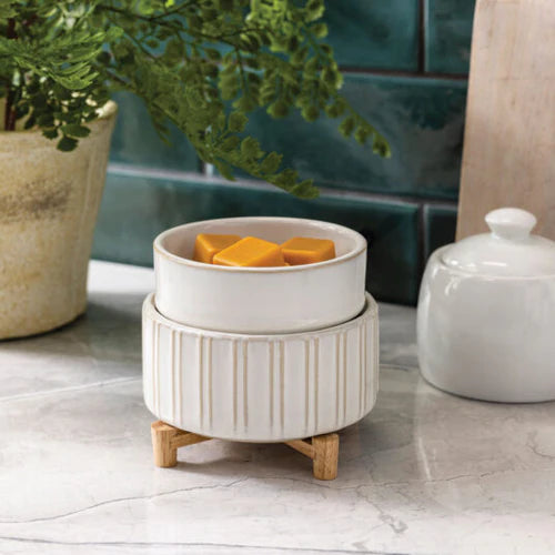 White ceramic planter with decorative stand on a marble surface, with a plant and other decor items in the background.
