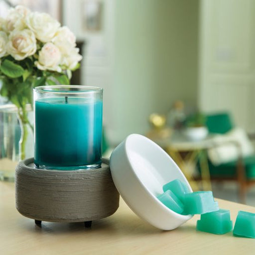 Blue candle in a warmer with teal wax melts on a table with a blurred indoor background