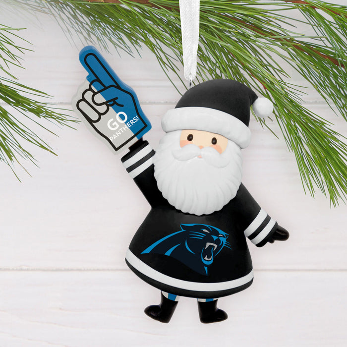 A Carolina Panthers Santa Claus hanging ornament styled with pine branches on a white wood background. The ornament depicts Santa in a black and white uniform with the team logo, holding a blue foam finger that says 'GD Panthers'.