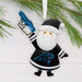 A Carolina Panthers Santa Claus hanging ornament styled with pine branches on a white wood background. The ornament depicts Santa in a black and white uniform with the team logo, holding a blue foam finger that says 'GD Panthers'.