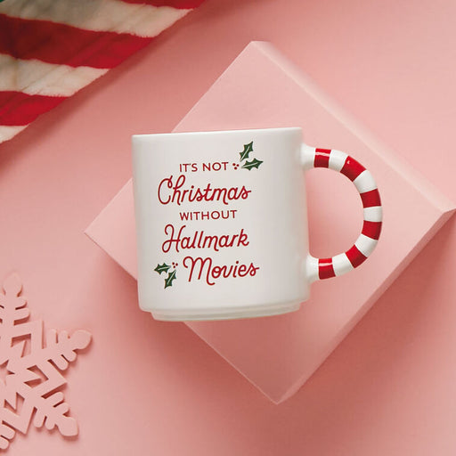 White mug with red text and candy cane handle on a pink background