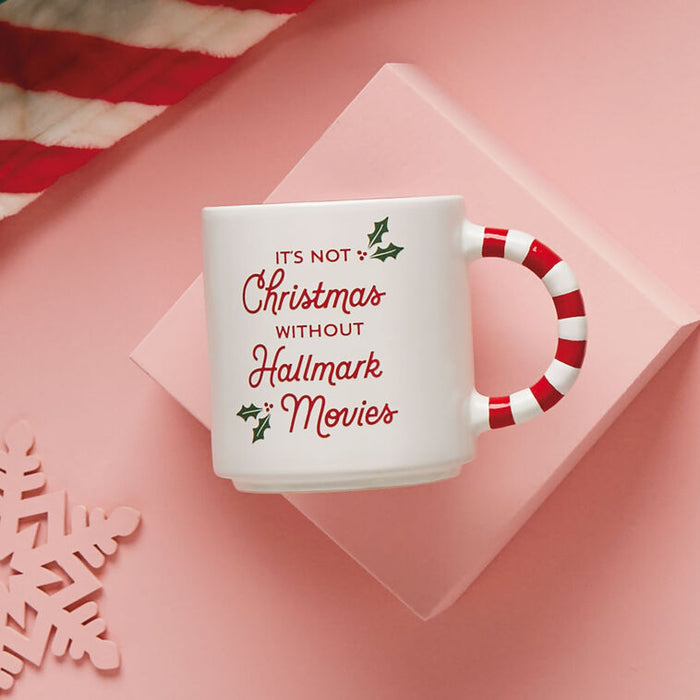 White mug with red text and candy cane handle on a pink background