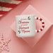 White mug with red text and candy cane handle on a pink background