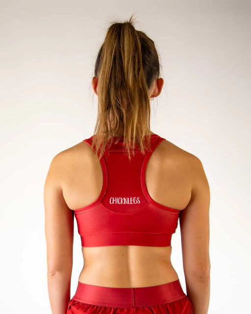 Person wearing a red sports bra with 'CHICKENLESS' branding on a plain background