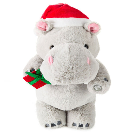 Plush hippo toy wearing a Santa hat and holding a gift on a white background