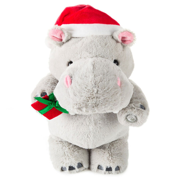 Plush hippo toy wearing a Santa hat and holding a gift on a white background