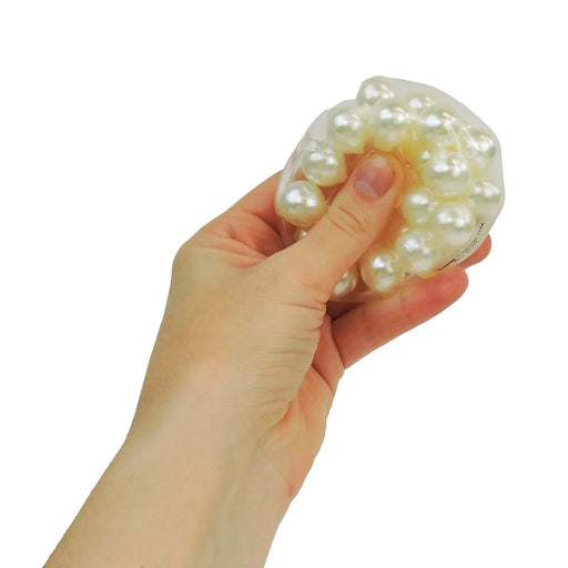 A hand squeezing a white, pearlescent stress toy made of translucent silicone and faux pearls, shown against a plain white background.