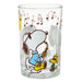 A clear glass drinking tumbler featuring a cartoon print of Snoopy playing a gold saxophone with Woodstock, decorated with brown musical notes against a white background.
