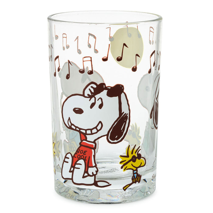A clear glass drinking tumbler featuring a cartoon print of Snoopy wearing a red sweater that says 'ICE COOL' and Woodstock, with musical notes and gray clouds on a white background.