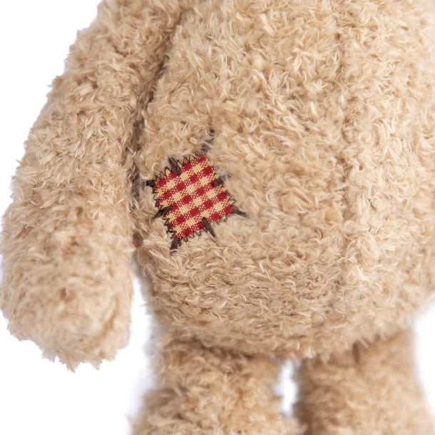 Close-up of a beige teddy bear with a red and yellow checkered patch on a white background