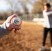 Hand holding a baseball with 'Kore' branding on a blurred outdoor background