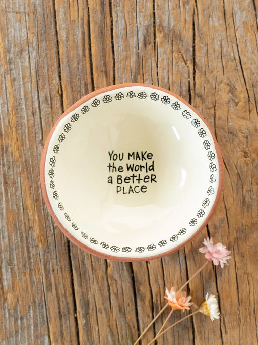 Decorative plate with 'You make the world a better place' text on a wooden surface with flowers.