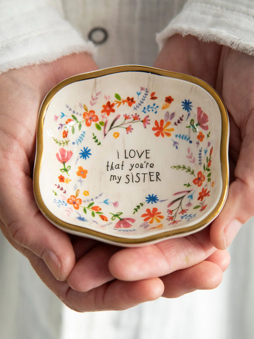 Small decorative dish held in hands with floral design and text 'I love that you're my sister'.