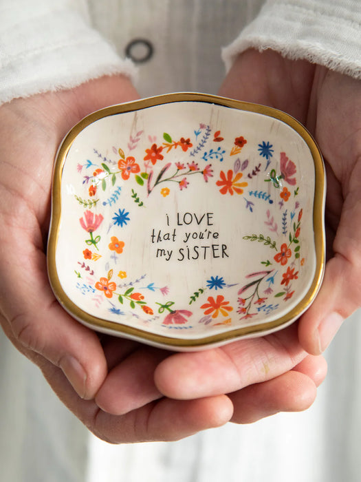 Small decorative dish held in hands with floral design and text 'I love that you're my sister'.