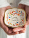 Small decorative dish held in hands with floral design and text 'I love that you're my sister'.