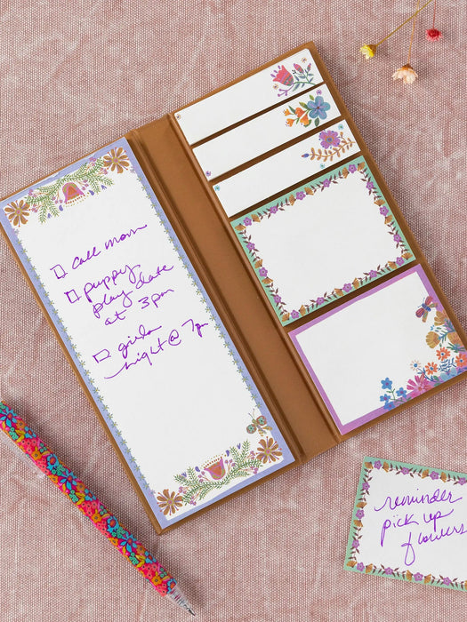 Notebook with floral design on the cover and pages, with a pen on a pink background.