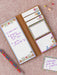 Notebook with floral design on the cover and pages, with a pen on a pink background.