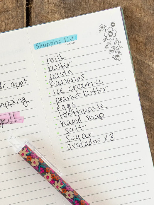 Handwritten shopping list on a notebook with a floral pen.