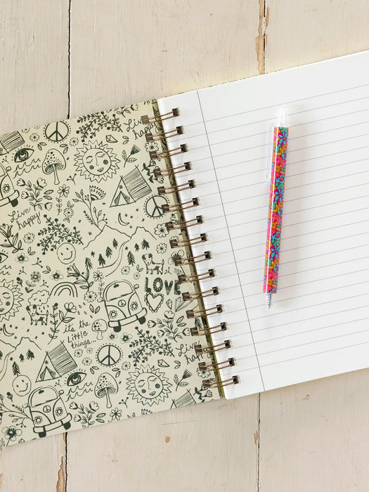 Open notebook with doodles on the cover and a colorful pen on a wooden surface