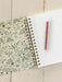 Open notebook with doodles on the cover and a colorful pen on a wooden surface