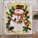 Decorative blanket with a snowman design featuring a scarf, hat, and holly leaves in a room setting.