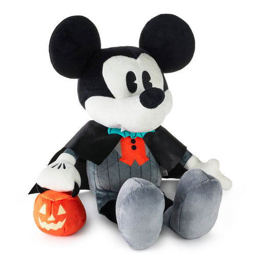 A Mickey Mouse plush toy dressed as a vampire, holding a small orange jack-o'-lantern. The plush features black and white fur-like fabric, gray pants, a black cape, a red bow tie, and a small teal collar accent.