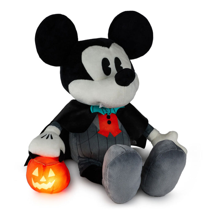 A Mickey Mouse plush toy dressed as a vampire, sitting and holding a glowing jack-o'-lantern pumpkin. The plush features black and white fur, a black cape, a red bow tie, and gray pants, set against a plain white background.