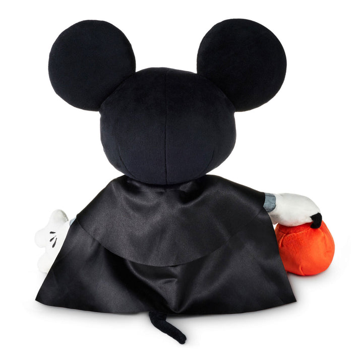 A Mickey Mouse plush toy shown from the back, wearing a black satin cape and holding an orange pumpkin, set against a plain white background.