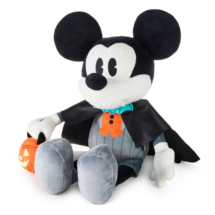 A Mickey Mouse plush toy dressed in a Halloween vampire costume, featuring a black cape, gray pinstripe shirt, orange ghost accessory, and holding an orange jack-o'-lantern, set against a plain white background.