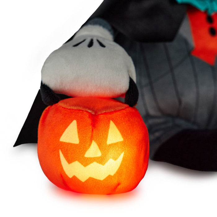 A plush Halloween decoration featuring a glowing orange jack-o'-lantern pumpkin in the foreground, with a white ghost character peeking out from behind a black cape and gray striped body on a white background.