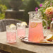 Pink lemonade in glasses and a pitcher on a stone surface with a garden background