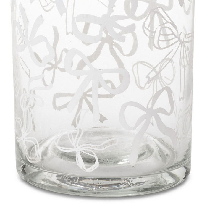 A clear glass tumbler with an etched pattern of white bows and ribbons, shown against a plain white background.