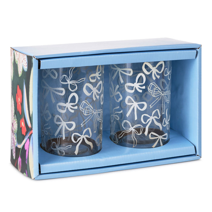 A pair of clear glass tumblers with white bow patterns, presented inside a light blue gift box with a floral-patterned side panel.