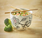 White bowl with floral design containing a salad, accompanied by chopsticks and broccoli on a wooden surface.